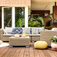 Beige garden furniture with striped pillows on a wooden terrace with pink flowers and poufs